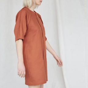 Blonde woman is swinging her arms and wears a slightly loose burnt orange dress with raglan sleeves. The Moonless Night Dress in Burnt Orange features a sleek stitching detail down the front. The dress is from Canadian designer Eve Gravel.