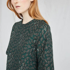 Red-haired woman wears an emerald top with intricate jacquard detailing. The Night Bird top is from Canadian designer Eve Gravel.