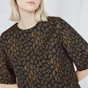 Blonde woman wears an orange and black top with intricate jacquard detailing. The Night Bird top is from Canadian designer Eve Gravel.