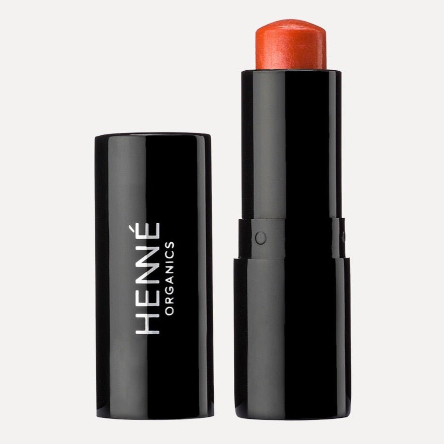 A tube of bright orange lip tint. The Luxury Lip Tint in Coral is designed by Henné Organics and made in the USA.