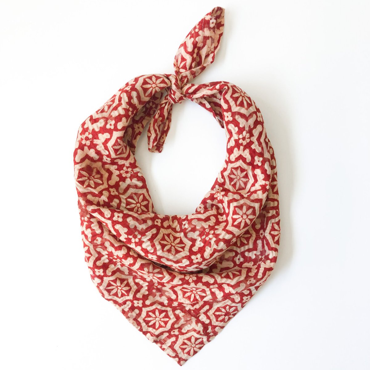 A red and cream patterned bandana, folded over and tied in a knot. Block printed by hand, the Fez Bandana from Maelu is designed in Portland, Oregon and handmade in India.