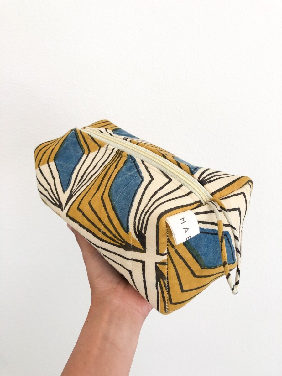 A person holding a yellow, cream and blue patterned cosmetic bag. The Hattie Cosmetic Bag from Maelu is designed in Portland, Oregon and printed and made in India.
