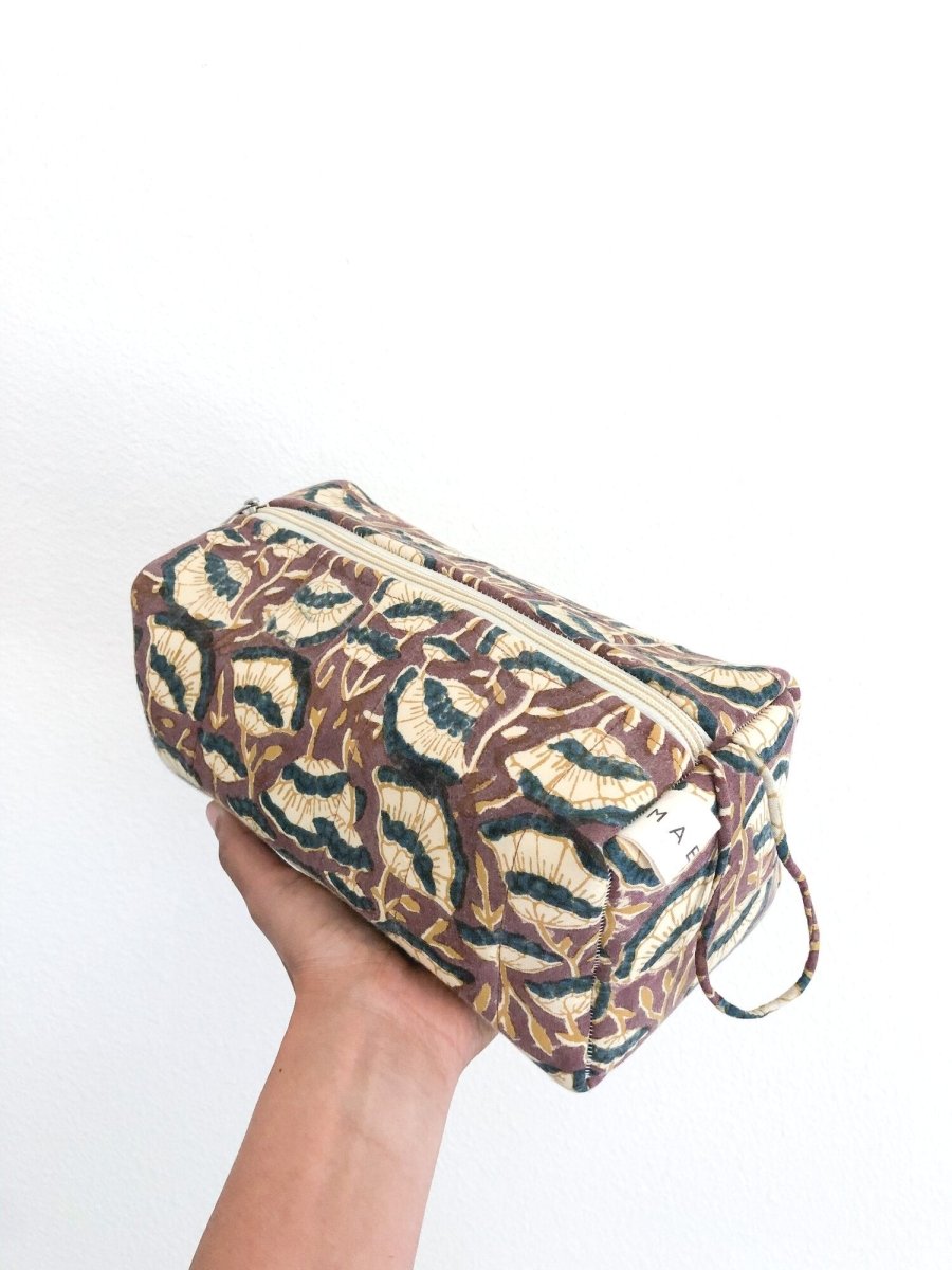 A person holding a brown, cream and dark blue floral patterned cosmetic bag. The Lena Cosmetic Bag from Maelu is designed in Portland, Oregon and printed and made in India.