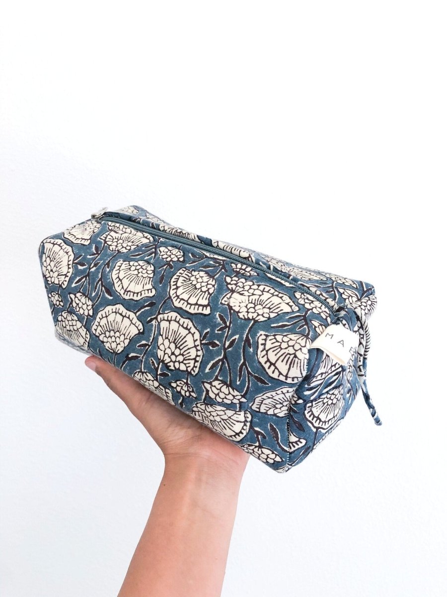 A person holding a blue and cream floral patterned cosmetic bag. The Poppy Cosmetic Bag from Maelu is designed in Portland, Oregon and printed and made in India.