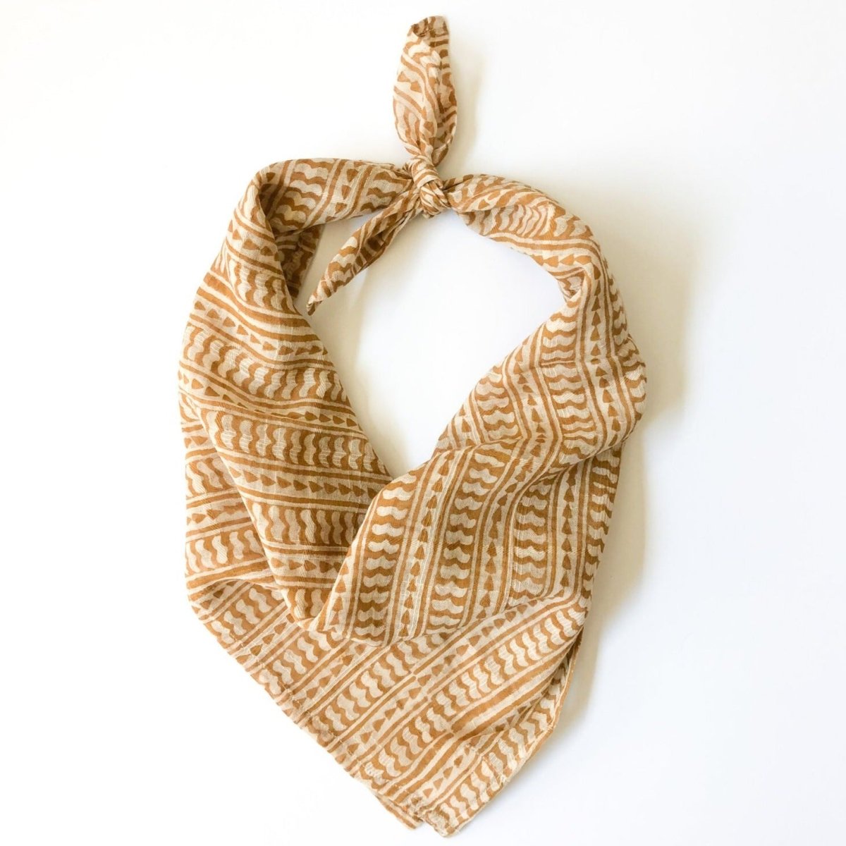 A yellow and cream bandana, folded over and tied in a knot. Block printed by hand, the Mustard Bandana from Maelu is designed in Portland, Oregon and handmade in India.
