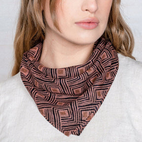 A woman wears a pink printed bandana around her neck. The Rumi Bandana from Maelu is designed in Portland, Oregon and made and printed by hand in India.