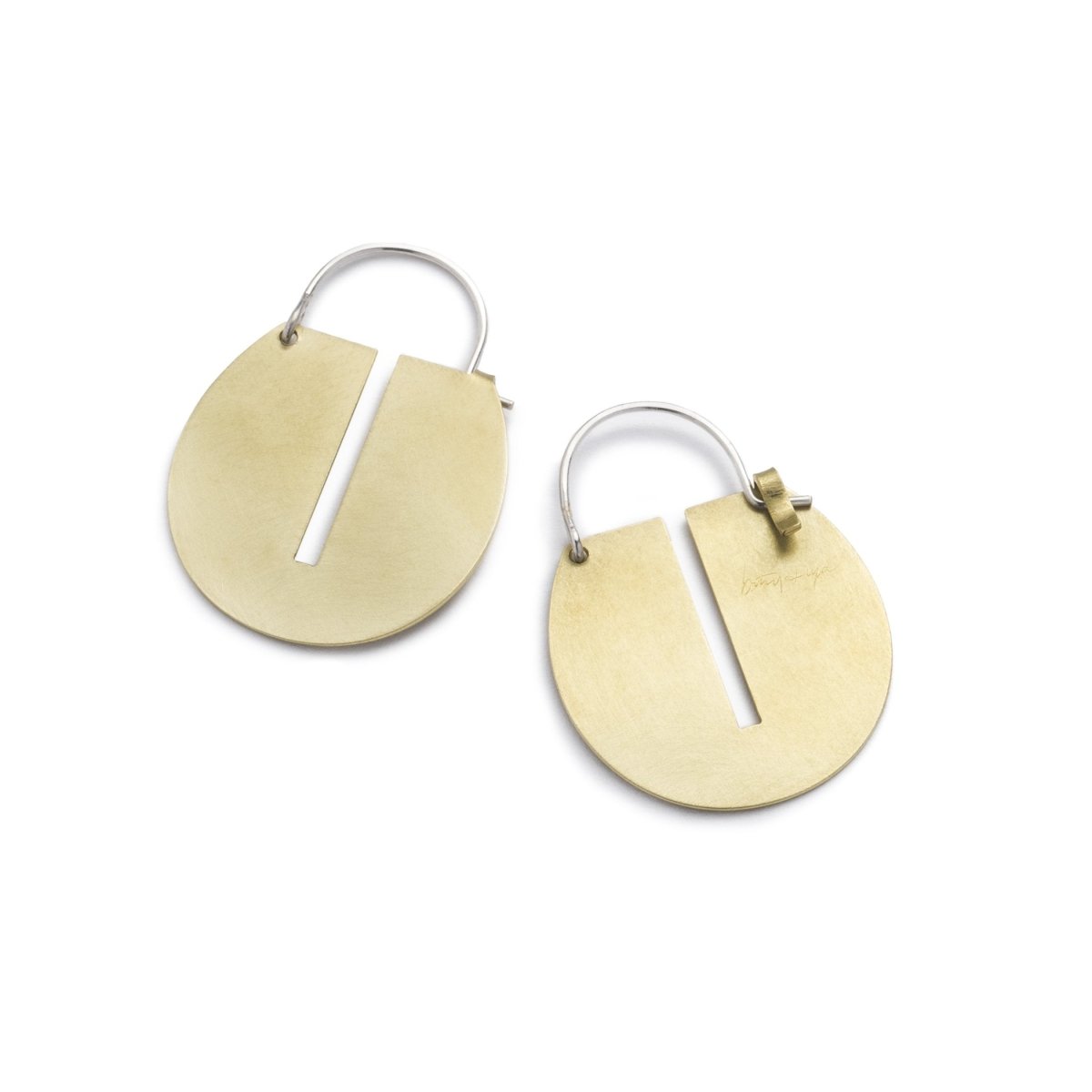 Small, round, brushed brass disc hoop earrings with a thin, rectangular cutout running down the center of the discs, and short, sterling silver earring wires that latch to the back of the discs. Hand-crafted in Portland, Oregon.
