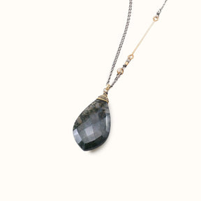 A blue, grey and black agate pendent hangs from a wrapping of gold-fill and sterling silver wire. Three tiny gold-fill hoops connect the pendant to a sterling silver chain with a gold filled accent bar. The Alloria Moss Agate Necklace is designed and handmade by Amy Olson in Portland, OR.