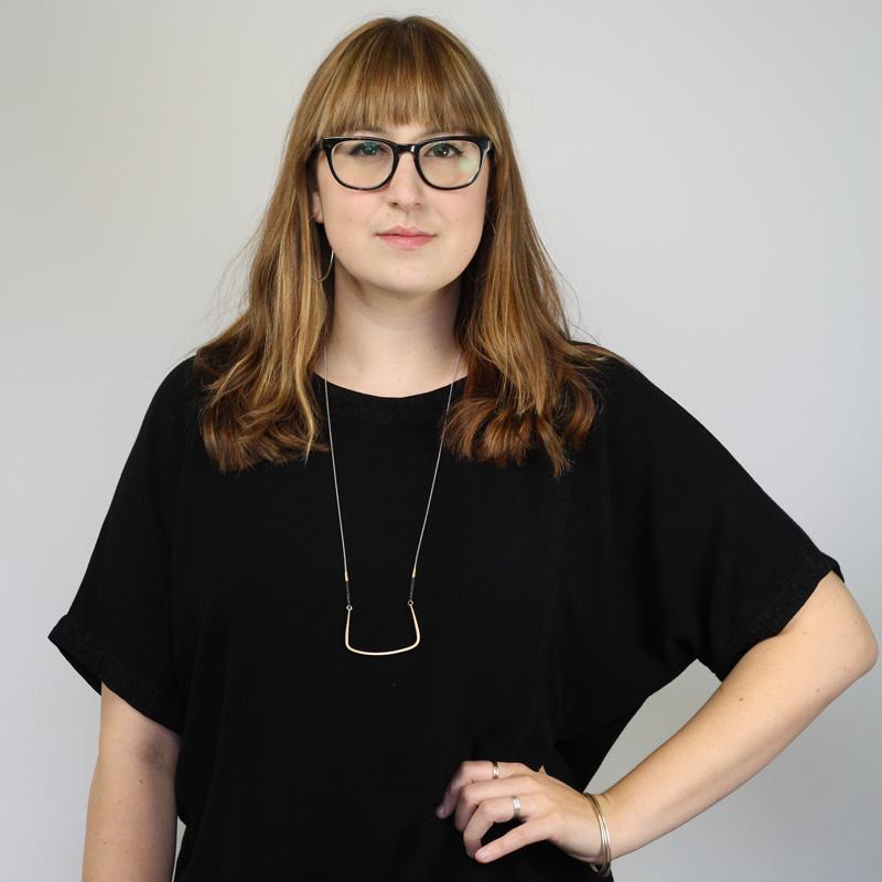 The elegant and flattering betsy & iya Nuwe necklace, styled on a model with glasses, sandy-blond bangs, and a black tunic.