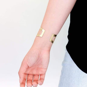 Adjustable side of the betsy & iya brass Pennybacker cuff bracelet, pictured on a model wearing jeans and a black shirt.