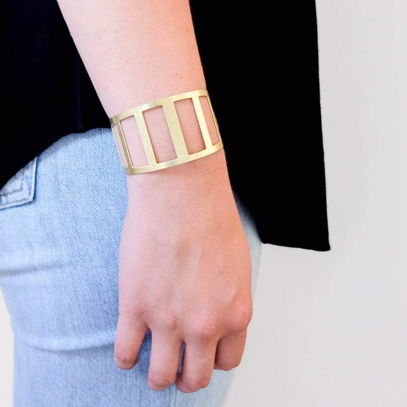 Modern, minimal, adjustable brass cuff modeled after the Pennybacker Bridge, pictured on a model wearing jeans and a black shirt.