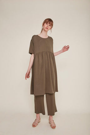 Red-haired woman wears a brown babydoll dress and matching pants. The Drapey Dress in Kaki is from designer Rita Row.