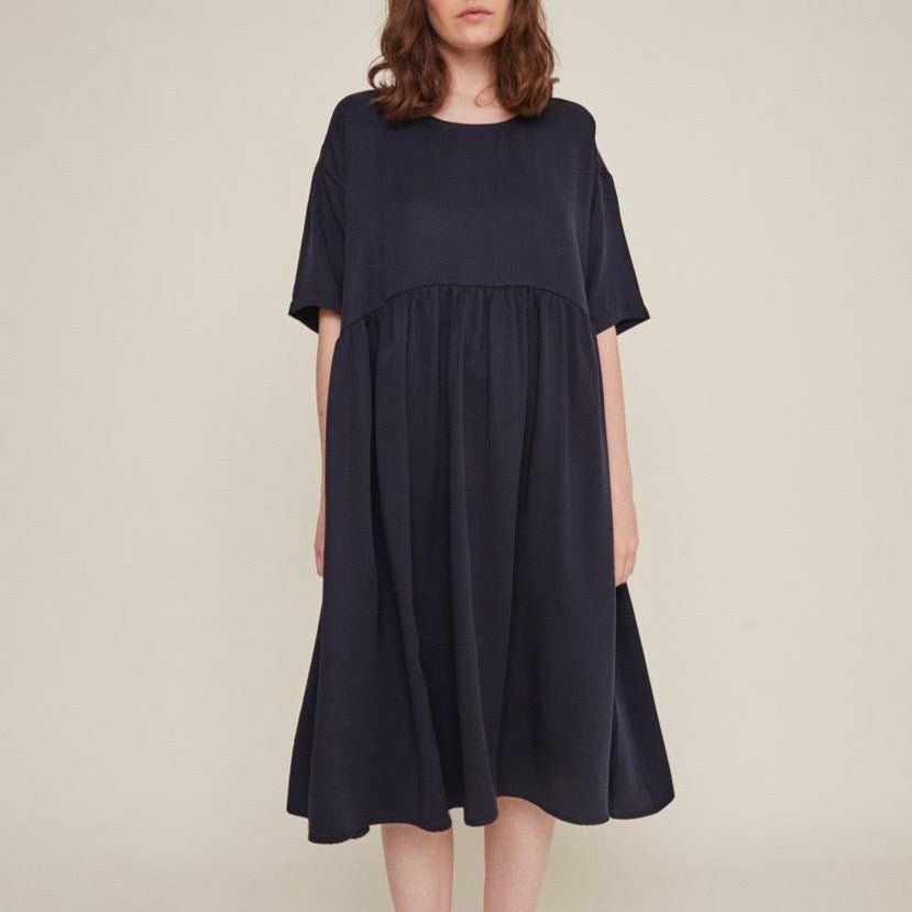 Red-haired woman wears a dark navy babydoll dress. The Drapey Dress in Navy is from designer Rita Row.