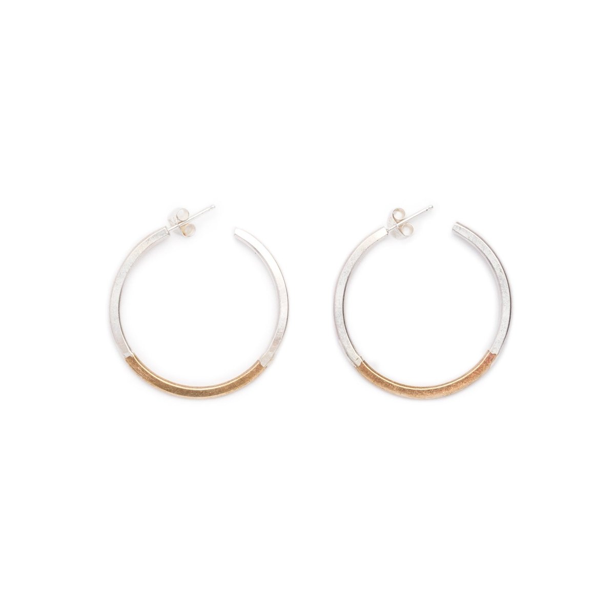 Small, minimalist, and lightweight hoop earrings of mixed brass and sterling silver hand-forged wire, with soldered sterling silver earring posts and sterling silver butterfly backings. Hand-crafted in Portland, Oregon.