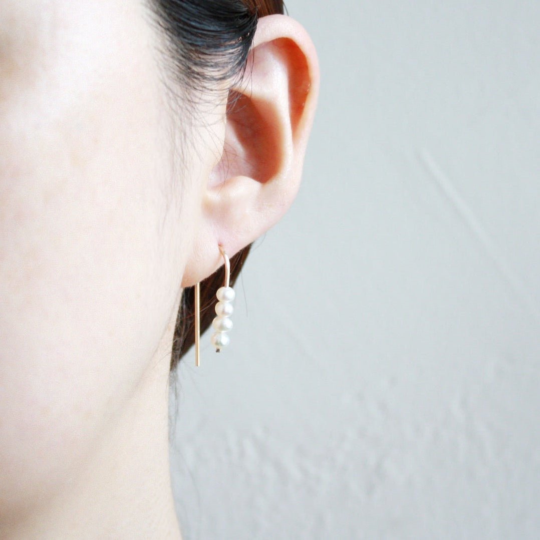 A model wears a rounded gold tone wire holds four petite freshwater pearls. The Short Arc Threader Earrings are designed and handcrafted by Hooks and Luxe in Jackson Heights, NY.