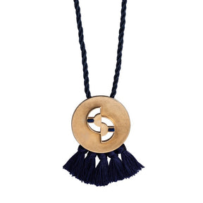 Circular, quarter-sized, cast-bronze pendant with curved cutouts, two rectangular, lapis lazuli inlays, and navy blue cotton fringe, threaded with a navy blue cotton rope. Hand-crafted in Portland, Oregon.