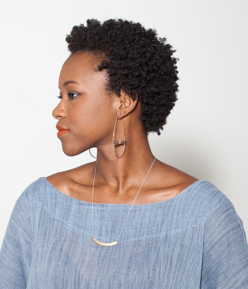 The 18 inch Humboldt Moon necklace, pictured on the profile of a model wearing betsy & iya bronze Alameda hoop earrings, a chambray top, and orange lipstick.