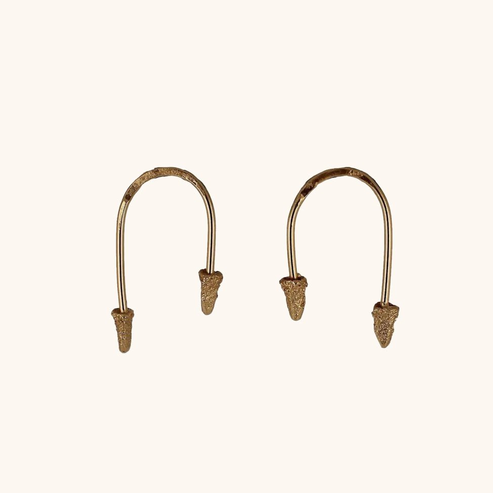 "U" shaped brass wire earrings with brass cones on each end. The brass cones are cast in cuttlefish bones. The Which Way to Go earrings are made by designer Lingua Nigra.